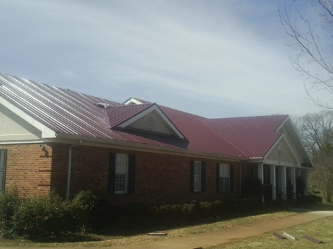 Red metal roof with gabled entries on a long brick building, from a Hail Damage Roof Repair job in Gatesville