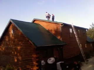 Crew on the ridge of a green metal roof on a two story log home in Gatesville