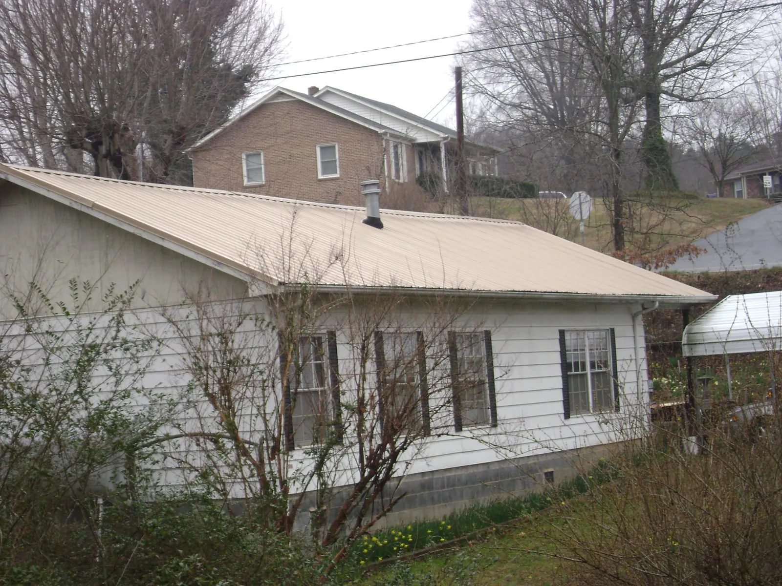 Tan metal roof on a white sided house set into a hillside — Commercial Roofing by Roofing Brothers in Gatesville