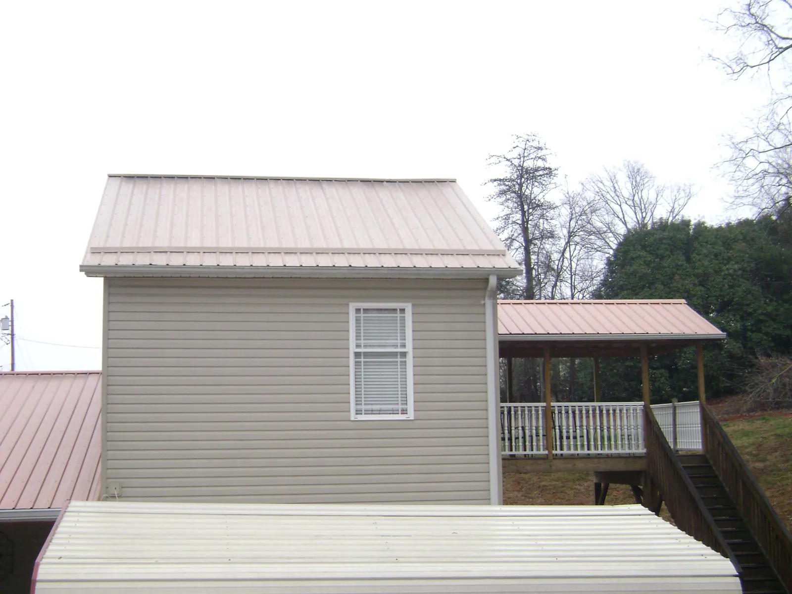 Tan metal roofs on a two story addition and attached porch, from a Roof Replacement job in Gatesville